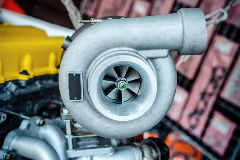 Metalowa turbosprężarka, kluczowy element silnika turbodoładowanego, z widocznymi łopatkami wirnika.