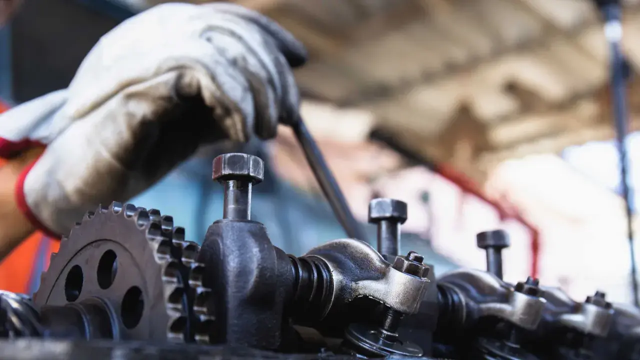 Mechanik w białej rękawicy pracuje nad elementami silnika. Zbliżenie na zawory i koło zębate. Czas potrzebny na planowanie głowicy zależy od wielu czynników.