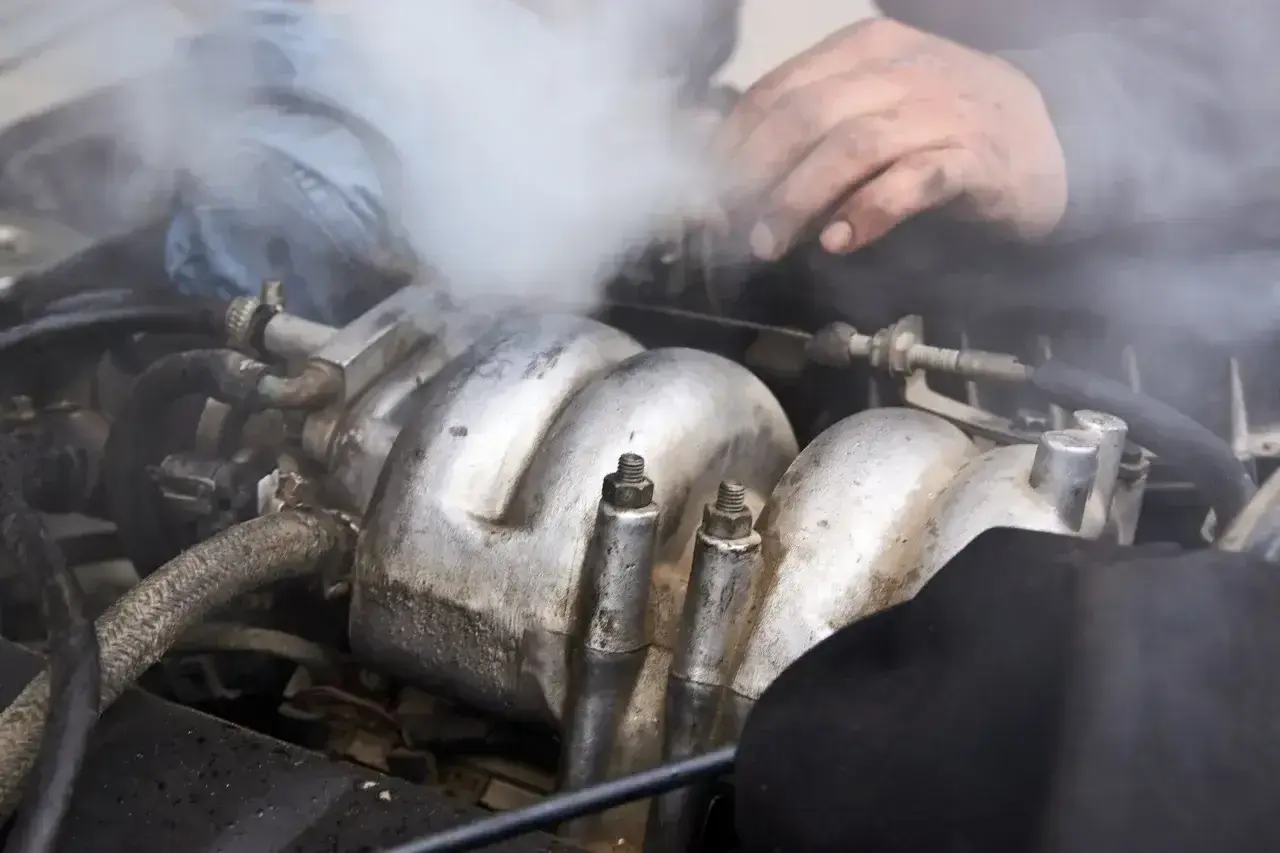 Mechanik próbuje naprawić silnik, z którego wydobywa się gęsty, biały dym.