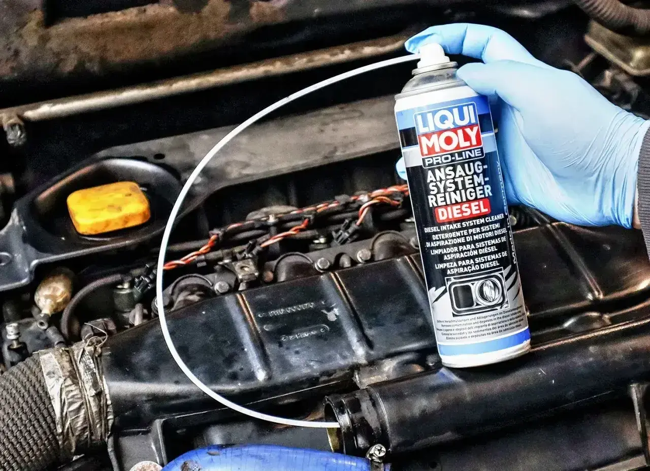Ręka w niebieskiej rękawiczce trzyma puszkę preparatu Liqui Moly, który rozpuszcza nagar w układzie dolotowym silnika Diesla.