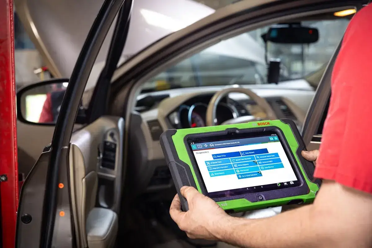Mechanik wykonuje diagnostykę komputerową samochodu za pomocą tabletu Bosch, sprawdzając jego systemy.